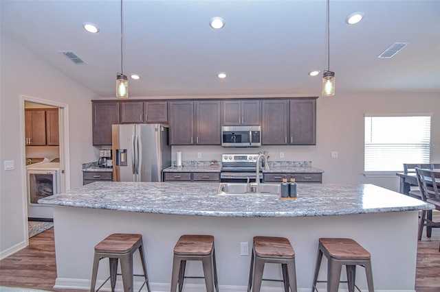 kitchen featuring independent washer and dryer, stainless steel appliances, light stone counters, and a center island with sink