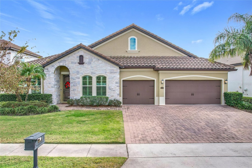 mediterranean / spanish-style house with a front lawn, decorative driveway, a tile roof, and stucco siding