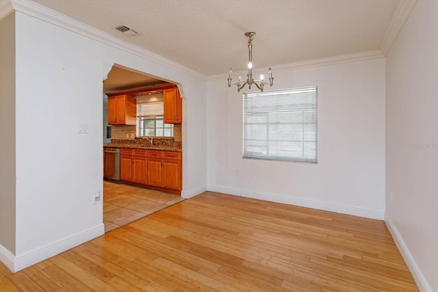 unfurnished dining area with a notable chandelier, sink, light wood-type flooring, and crown molding