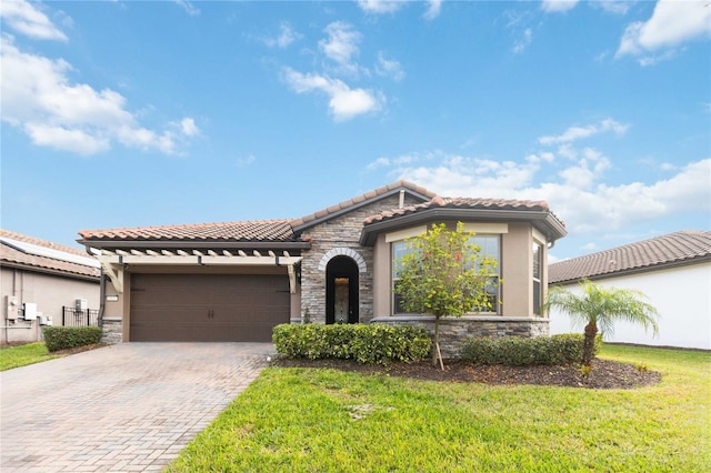 mediterranean / spanish house with an attached garage, stone siding, a tiled roof, decorative driveway, and a front lawn