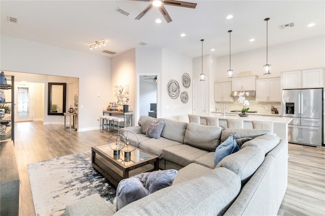 living room with ceiling fan, light hardwood / wood-style floors, and a high ceiling