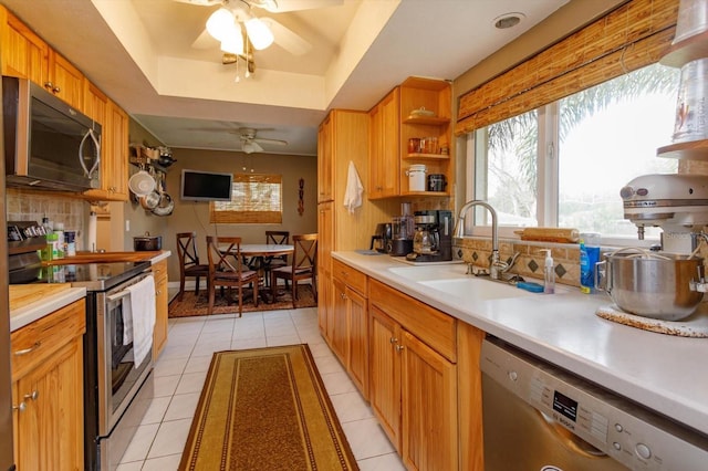 kitchen featuring a raised ceiling, sink, ceiling fan, light tile patterned flooring, and stainless steel appliances