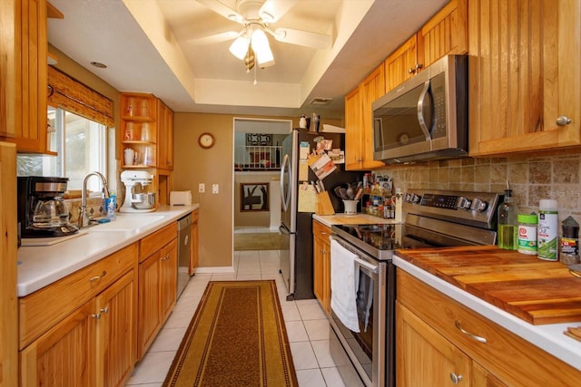 kitchen featuring backsplash, sink, light tile patterned floors, a tray ceiling, and stainless steel appliances