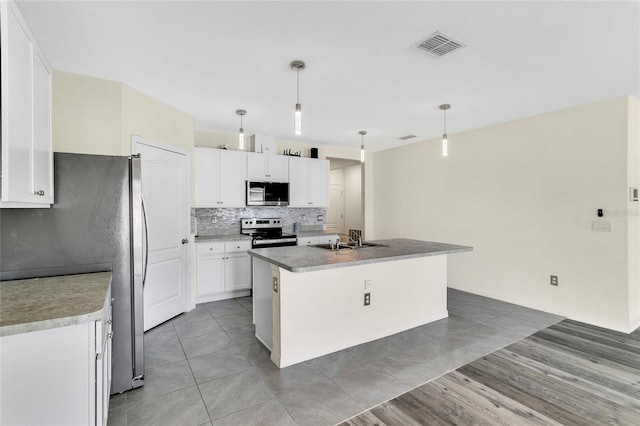 kitchen featuring stainless steel appliances, a kitchen island with sink, sink, white cabinetry, and hanging light fixtures