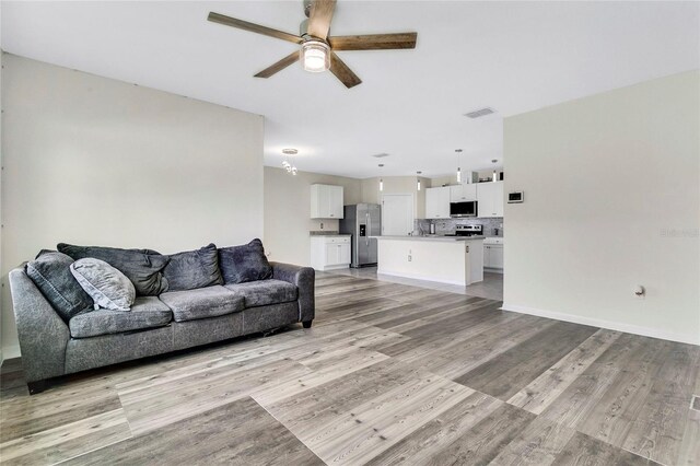 living room with a ceiling fan, visible vents, light wood finished floors, and baseboards