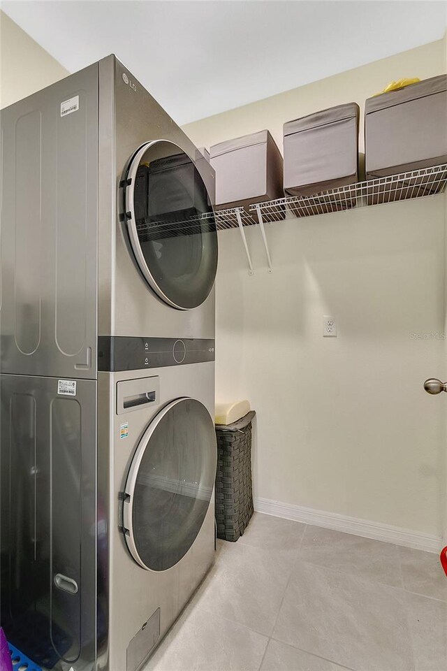 clothes washing area featuring laundry area, baseboards, tile patterned floors, and stacked washing maching and dryer