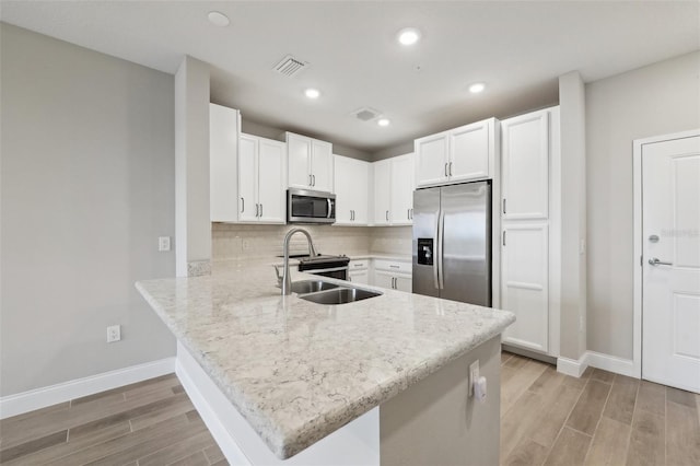 kitchen with backsplash, white cabinets, light hardwood / wood-style flooring, appliances with stainless steel finishes, and kitchen peninsula