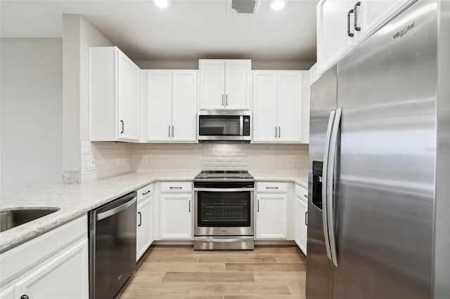 kitchen featuring backsplash, white cabinetry, stainless steel appliances, and light stone counters