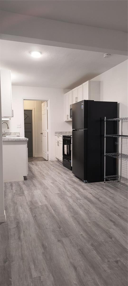 kitchen with white cabinets, sink, light hardwood / wood-style flooring, and black appliances