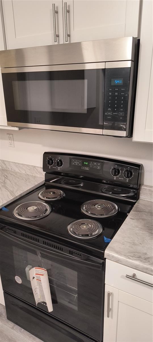 kitchen with black / electric stove, light stone countertops, white cabinets, and light hardwood / wood-style floors