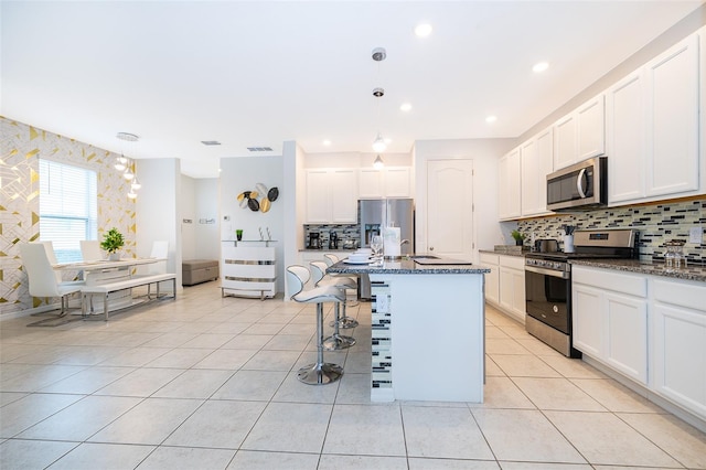 kitchen with a kitchen island with sink, white cabinets, dark stone counters, and appliances with stainless steel finishes