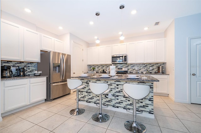 kitchen with a kitchen island with sink, dark stone counters, a kitchen breakfast bar, white cabinetry, and stainless steel appliances