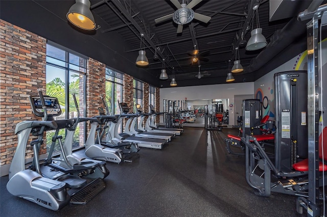 exercise room with ceiling fan, a towering ceiling, and brick wall