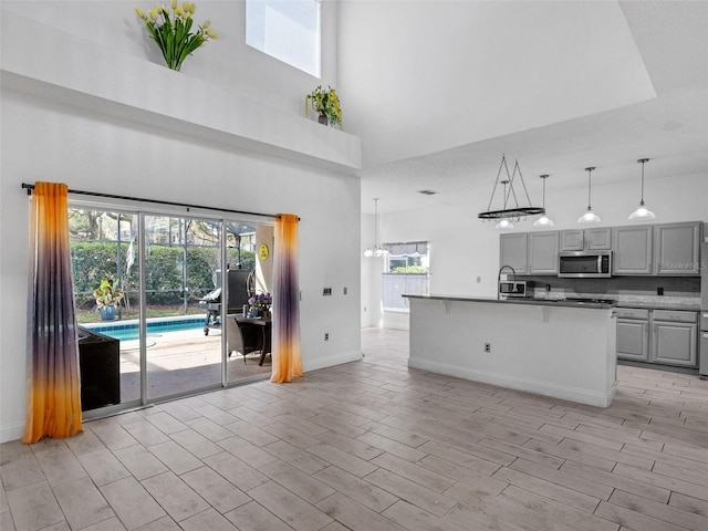 kitchen featuring sink, a high ceiling, decorative light fixtures, gray cabinets, and a kitchen island with sink