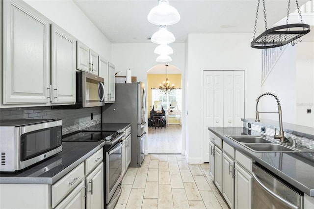 kitchen with gray cabinetry, sink, backsplash, pendant lighting, and appliances with stainless steel finishes