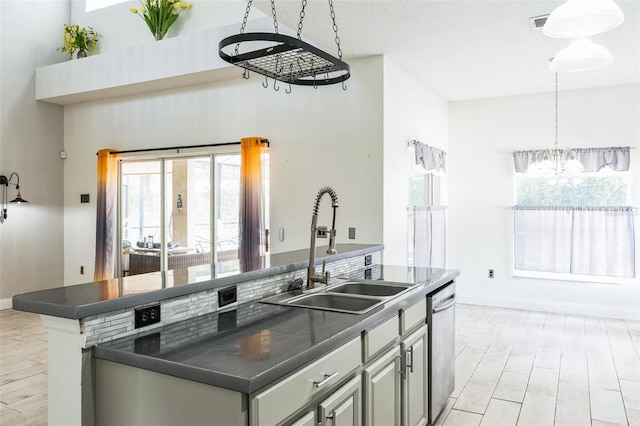 kitchen featuring sink, stainless steel dishwasher, a notable chandelier, decorative light fixtures, and a center island with sink