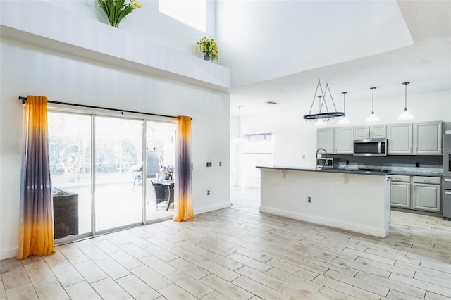 kitchen with a high ceiling, an island with sink, decorative light fixtures, gray cabinets, and a breakfast bar