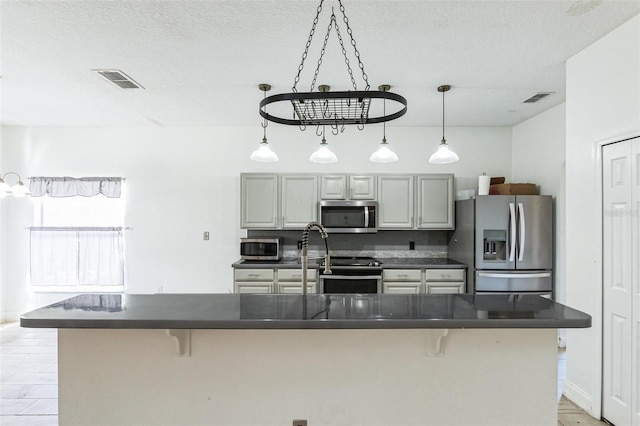 kitchen with a spacious island, a breakfast bar area, gray cabinets, a textured ceiling, and stainless steel appliances