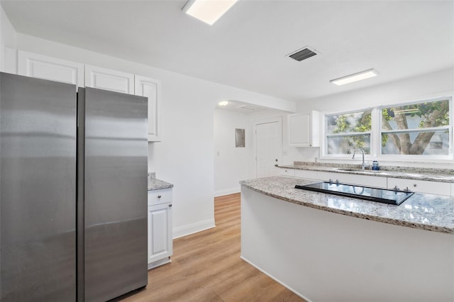 kitchen with light stone counters, freestanding refrigerator, white cabinetry, and visible vents