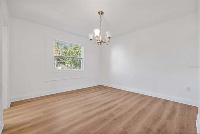 empty room featuring a chandelier, baseboards, and light wood finished floors