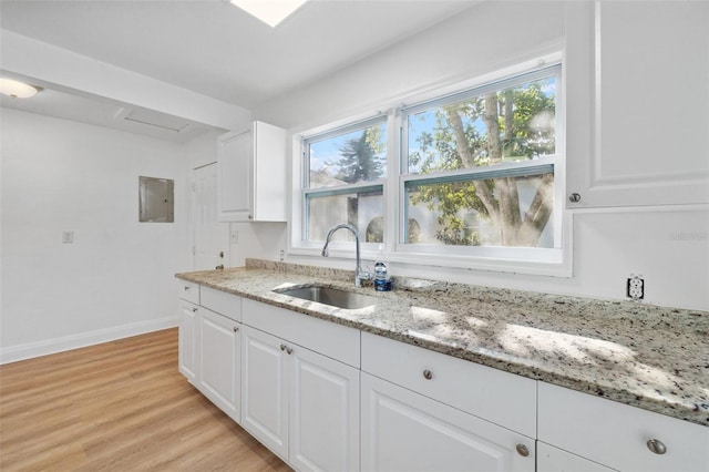 kitchen featuring light stone countertops, white cabinets, a sink, and light wood-style floors