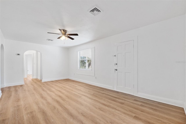 empty room featuring light wood-style flooring, arched walkways, ceiling fan, and visible vents