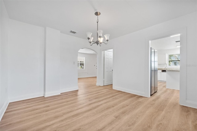 spare room with a chandelier, light wood-type flooring, baseboards, visible vents, and arched walkways