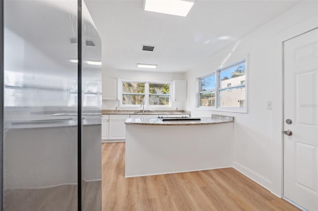 kitchen featuring white cabinets, visible vents, a peninsula, light wood finished floors, and freestanding refrigerator