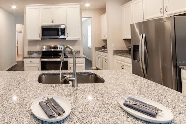 kitchen with white cabinets, sink, light stone countertops, and stainless steel appliances