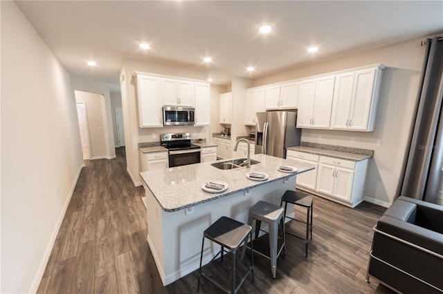 kitchen with light stone countertops, white cabinetry, sink, stainless steel appliances, and an island with sink