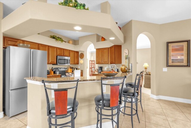 kitchen featuring a breakfast bar, light stone countertops, light tile patterned flooring, kitchen peninsula, and stainless steel appliances