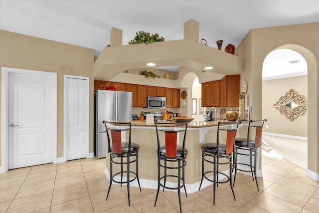 kitchen with light stone countertops, kitchen peninsula, a breakfast bar, light tile patterned floors, and appliances with stainless steel finishes