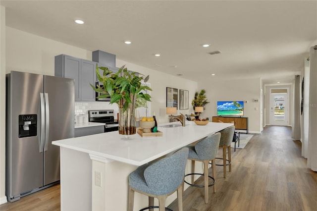 kitchen with gray cabinetry, sink, stainless steel refrigerator with ice dispenser, range with electric stovetop, and an island with sink