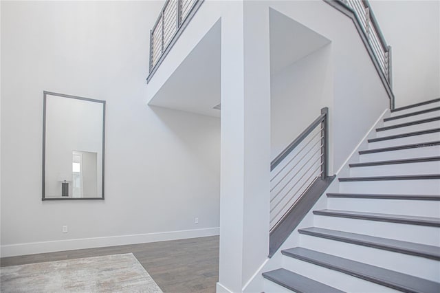 stairs with a high ceiling, baseboards, and wood finished floors