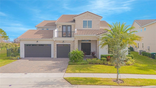 mediterranean / spanish house with a tile roof, a front yard, stucco siding, decorative driveway, and a balcony