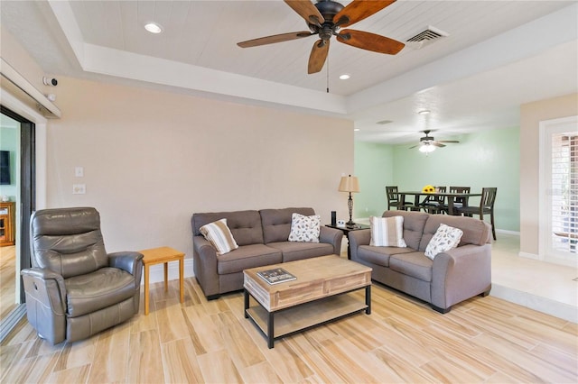 living room featuring a raised ceiling, ceiling fan, and light hardwood / wood-style flooring