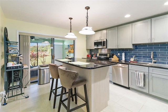 kitchen featuring appliances with stainless steel finishes, backsplash, decorative light fixtures, gray cabinets, and a kitchen island