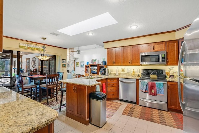 kitchen with sink, a skylight, light stone countertops, decorative light fixtures, and stainless steel appliances