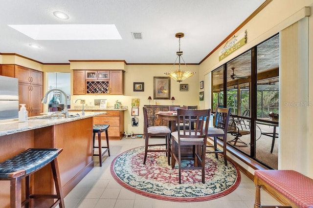 dining room with a skylight, sink, light tile patterned flooring, and ornamental molding