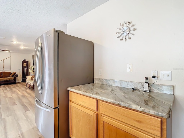 kitchen featuring stainless steel fridge, a textured ceiling, light hardwood / wood-style floors, and light stone counters