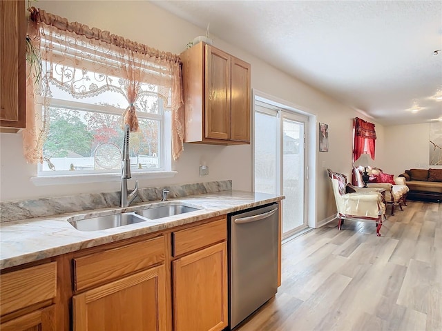 kitchen featuring stainless steel dishwasher, light stone countertops, light wood-type flooring, and sink