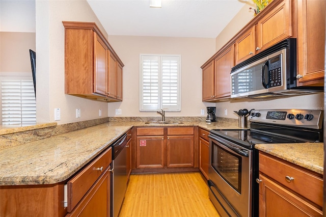 kitchen with light stone countertops, sink, stainless steel appliances, and light hardwood / wood-style floors