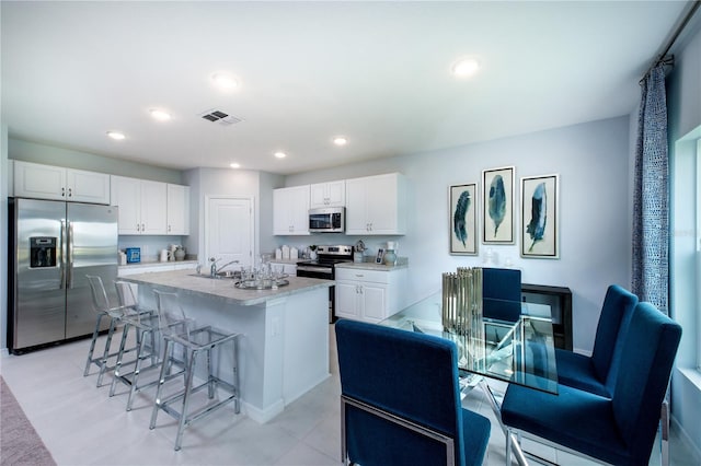 kitchen featuring white cabinets, a kitchen breakfast bar, sink, an island with sink, and appliances with stainless steel finishes