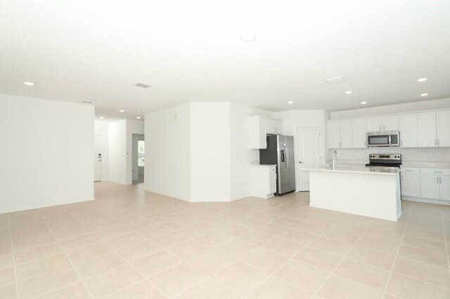 kitchen with white cabinetry, a kitchen island with sink, light tile patterned flooring, and appliances with stainless steel finishes