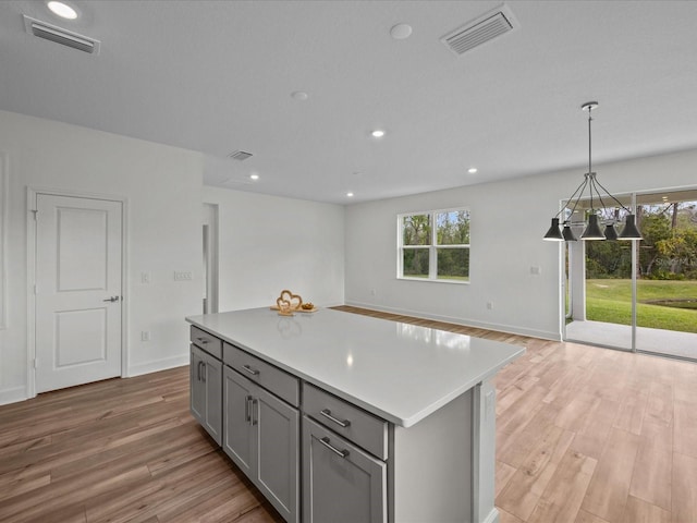 kitchen with pendant lighting, light hardwood / wood-style floors, a kitchen island, and gray cabinetry