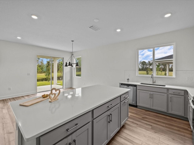 kitchen featuring a center island, backsplash, sink, light hardwood / wood-style flooring, and stainless steel dishwasher