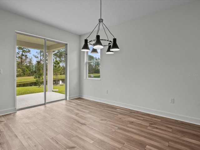 unfurnished dining area with light hardwood / wood-style floors, a water view, and a chandelier