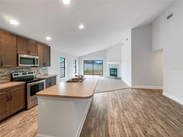 kitchen featuring sink, stainless steel appliances, tasteful backsplash, vaulted ceiling, and a kitchen island with sink