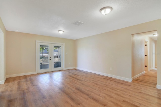 empty room with french doors, a textured ceiling, and light hardwood / wood-style flooring