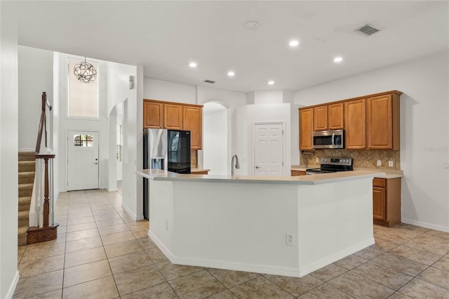 kitchen with stainless steel appliances, an island with sink, a chandelier, decorative backsplash, and light tile patterned flooring